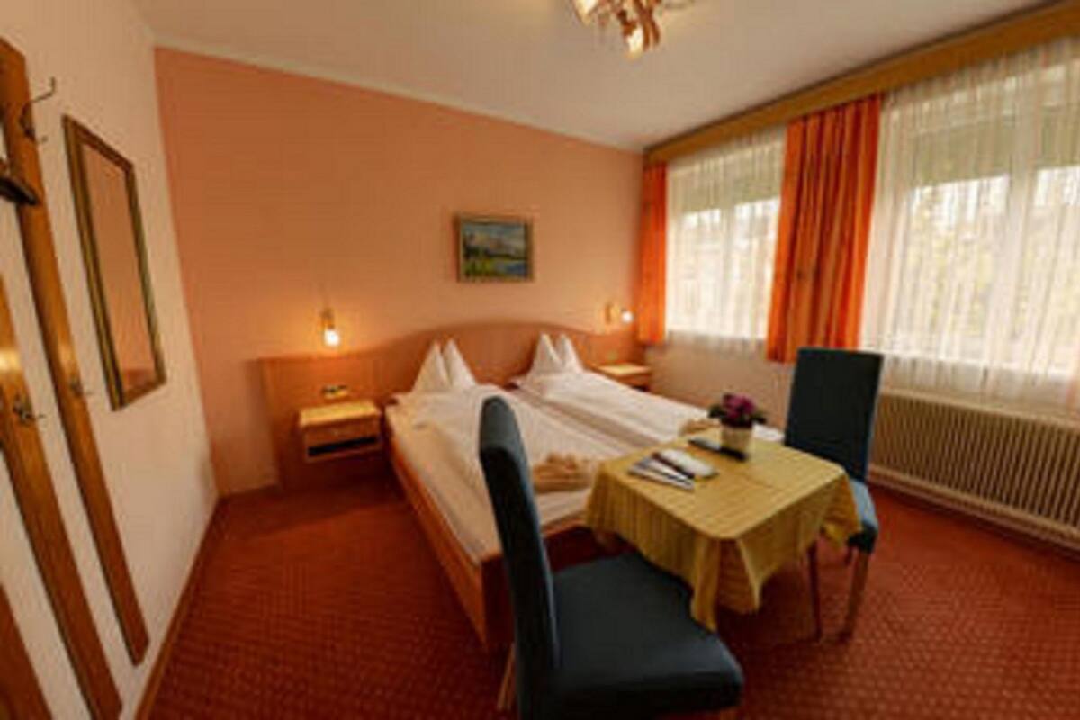 Ein Hotelzimmer mit Bett, Nachttisch, Stuhl, Tisch und einem Fenster mit Vorhängen.