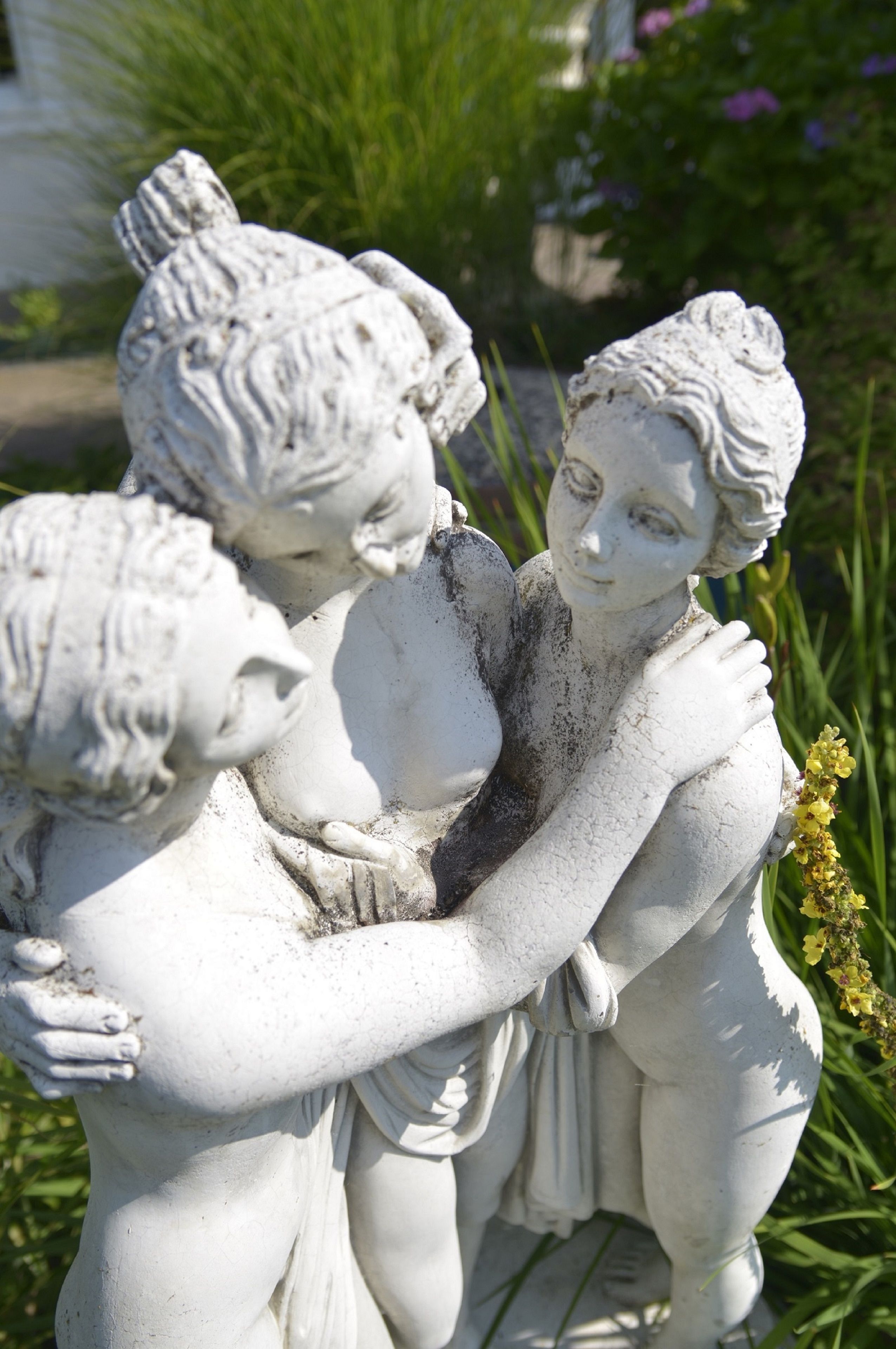 Une statue représentant deux personnages qui s’enlacent, entourée de verdure.