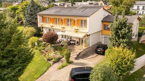 Ein zweistöckiges Haus mit Balkon, umgeben von viel Grün und einer Berglandschaft.