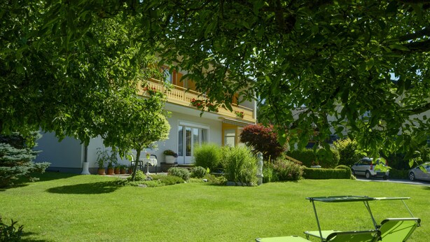 Ein gepflegter Rasen mit einem grünen Liegestuhl und einem Tisch, ein weißes Gebäude mit Balkon und eine Statue im Garten.