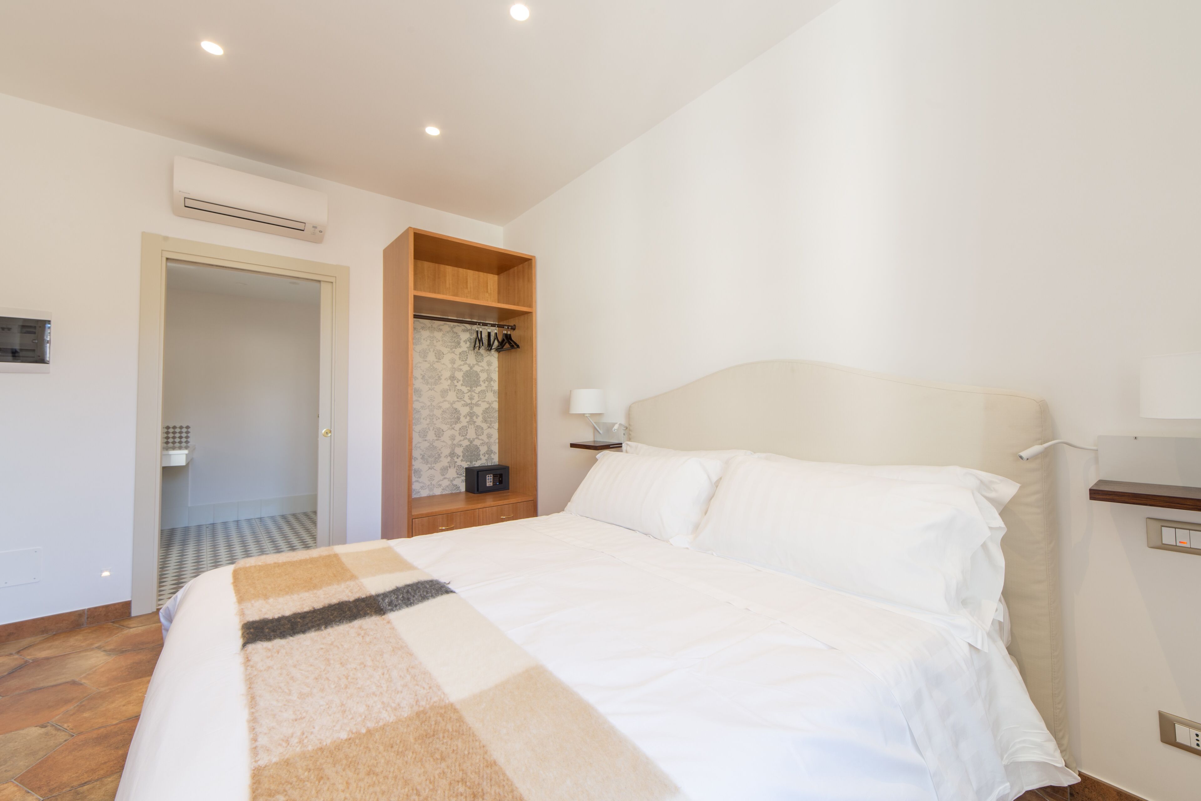 Une chambre d’hôtel équipée d’un lit, d’une armoire, d’une table de chevet avec une lampe et d’un appareil de climatisation fixé au mur.