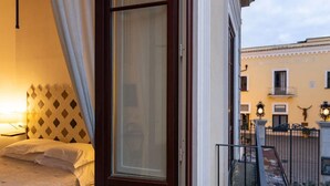 A hotel room with a bed, a window with curtains, and a view of the courtyard with buildings and a gate. - Residenza Il Campanile (Sorrento)