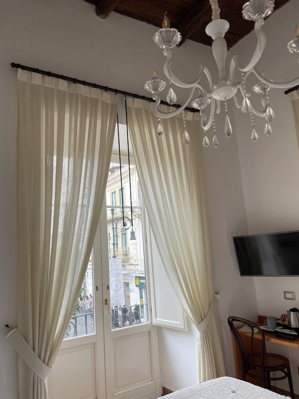 A room with a white door, a chandelier, a table with a TV, and a view of buildings outside.