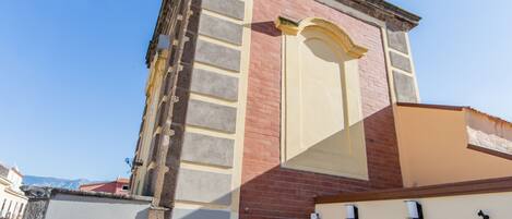 Un edificio con una torre de campanas, una puerta y un pequeño espacio con mesas al aire libre.