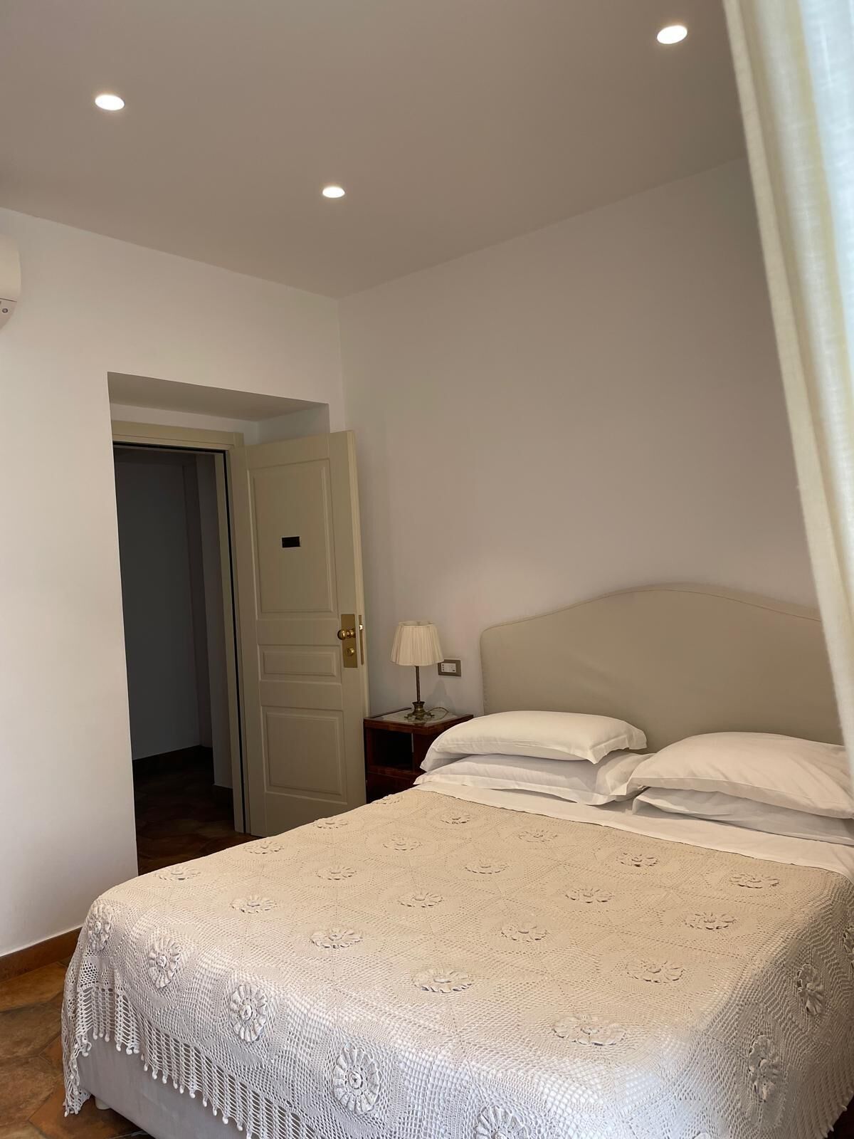 Un dormitorio con cama, mesita de noche, lámpara y puerta.