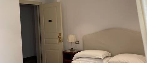 Un dormitorio con cama, mesita de noche, lámpara y puerta.