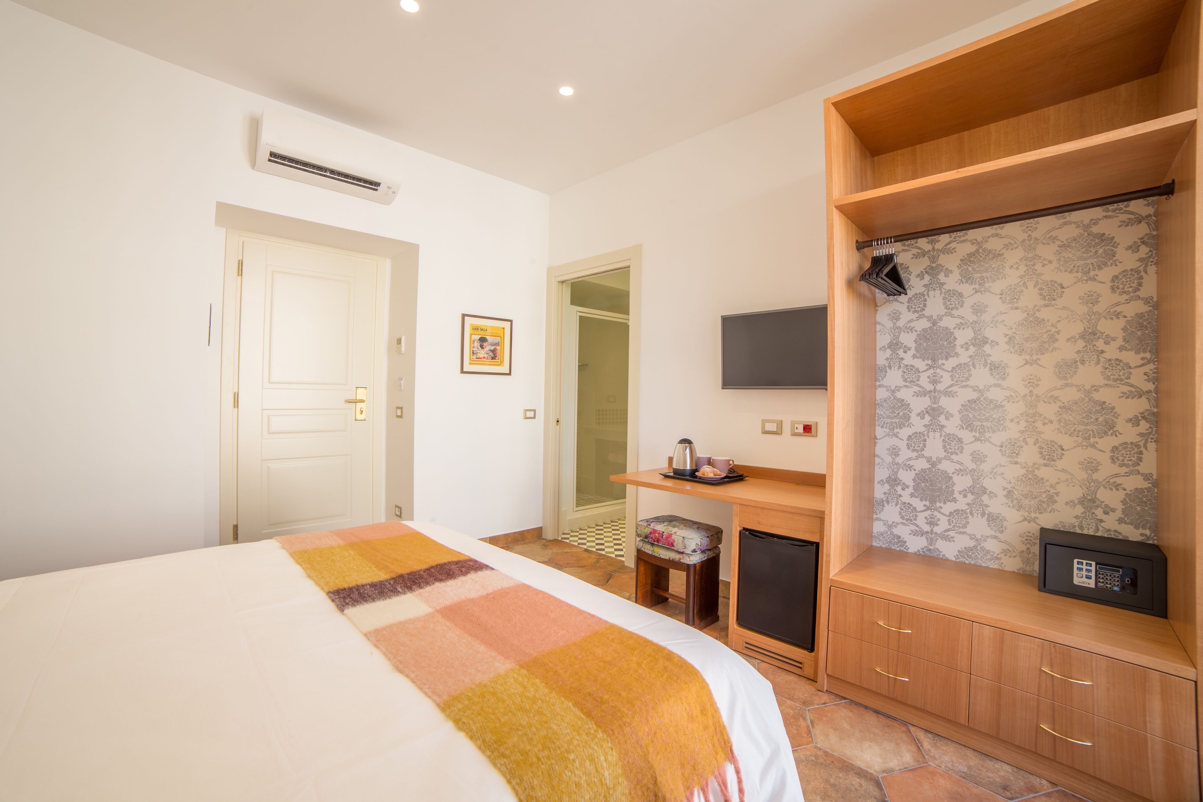 Een hotelkamer met een bed, een bureau met koffiezetapparaat, een televisie, een kledingkast en een klein krukje.