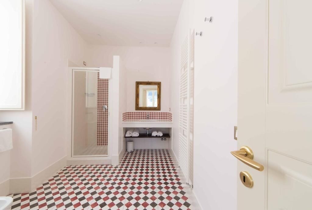 Une salle de bain avec un carrelage à motifs géométriques, un miroir au-dessus du lavabo et une porte dotée d’une poignée dorée.