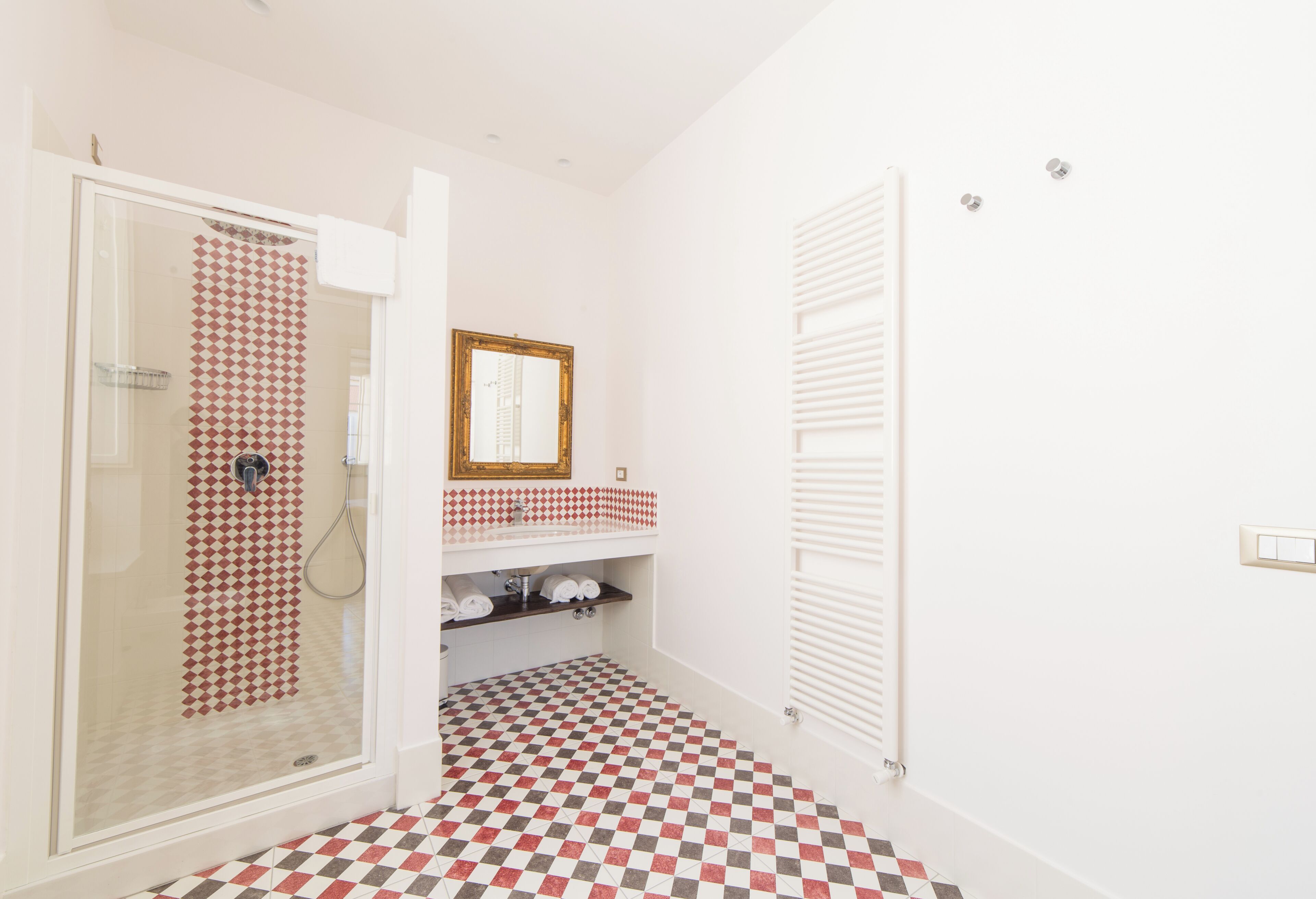 A bathroom with a checkered floor, a glass shower enclosure, a white sink with a mirror, and a white towel rack.