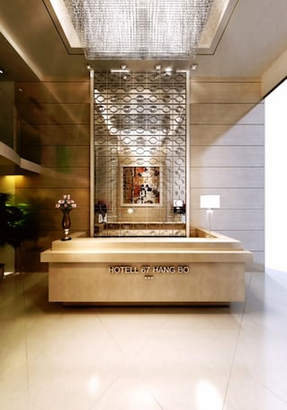 A modern reception desk with a chandelier above, a decorative screen, and a vase with flowers.