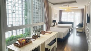 Ein Hotelzimmer mit zwei Betten, einem Schreibtisch mit Snacks, einem Fernseher und großen Fenstern mit Vorhängen.