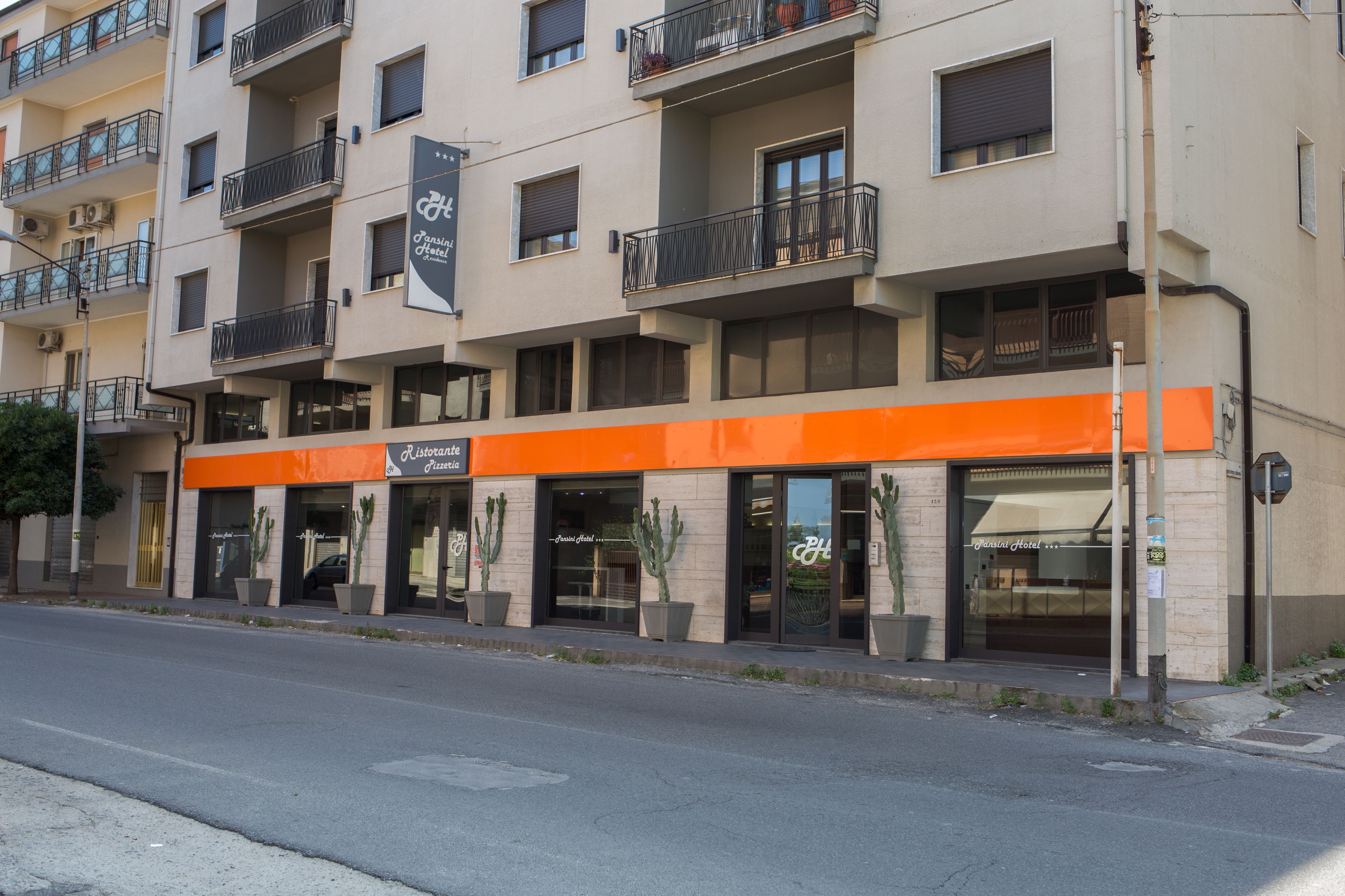 Ein mehrstöckiges Hotel mit auffälligem orangefarbenen Vordach, Balkonen und Topfpflanzen.