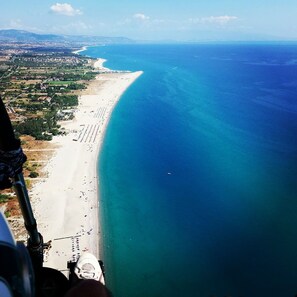 Vue aérienne d’une zone côtière avec une longue plage de sable et une mer bleue et limpide.