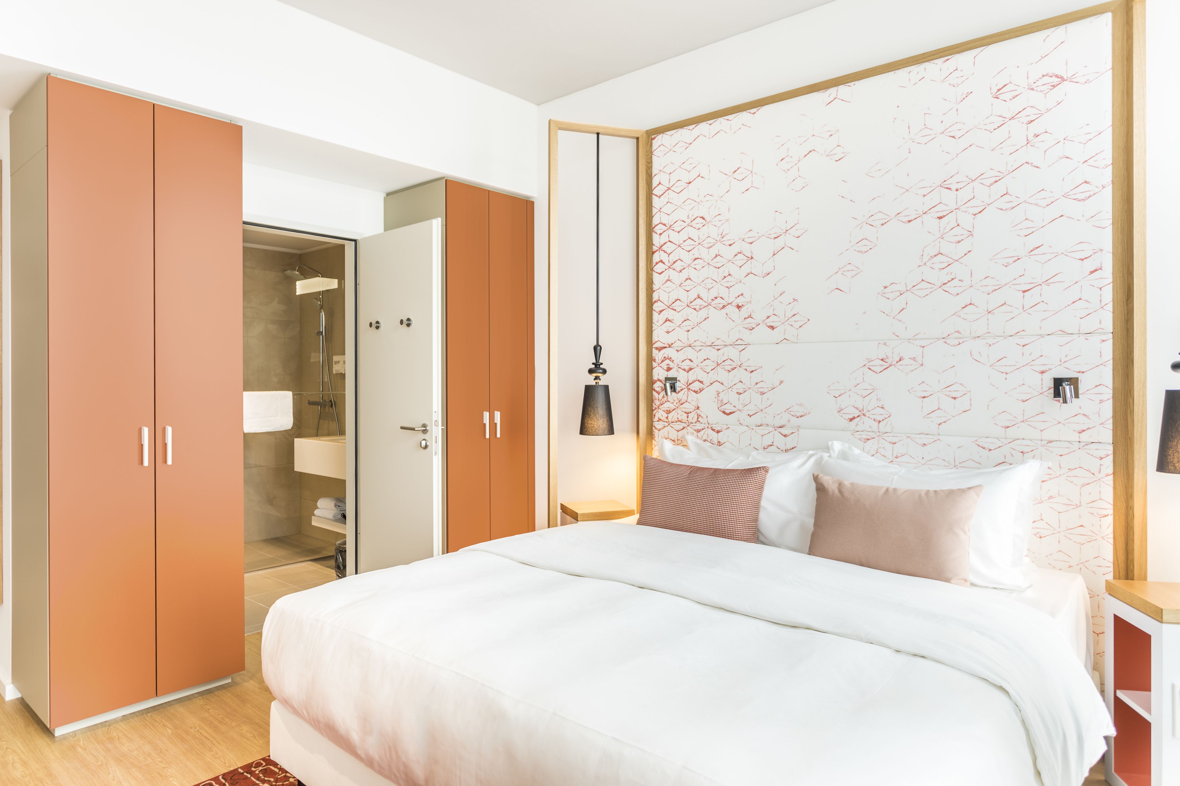 Een slaapkamer met een bed, een kledingkast, een douche en een muur met geometrische patronen.