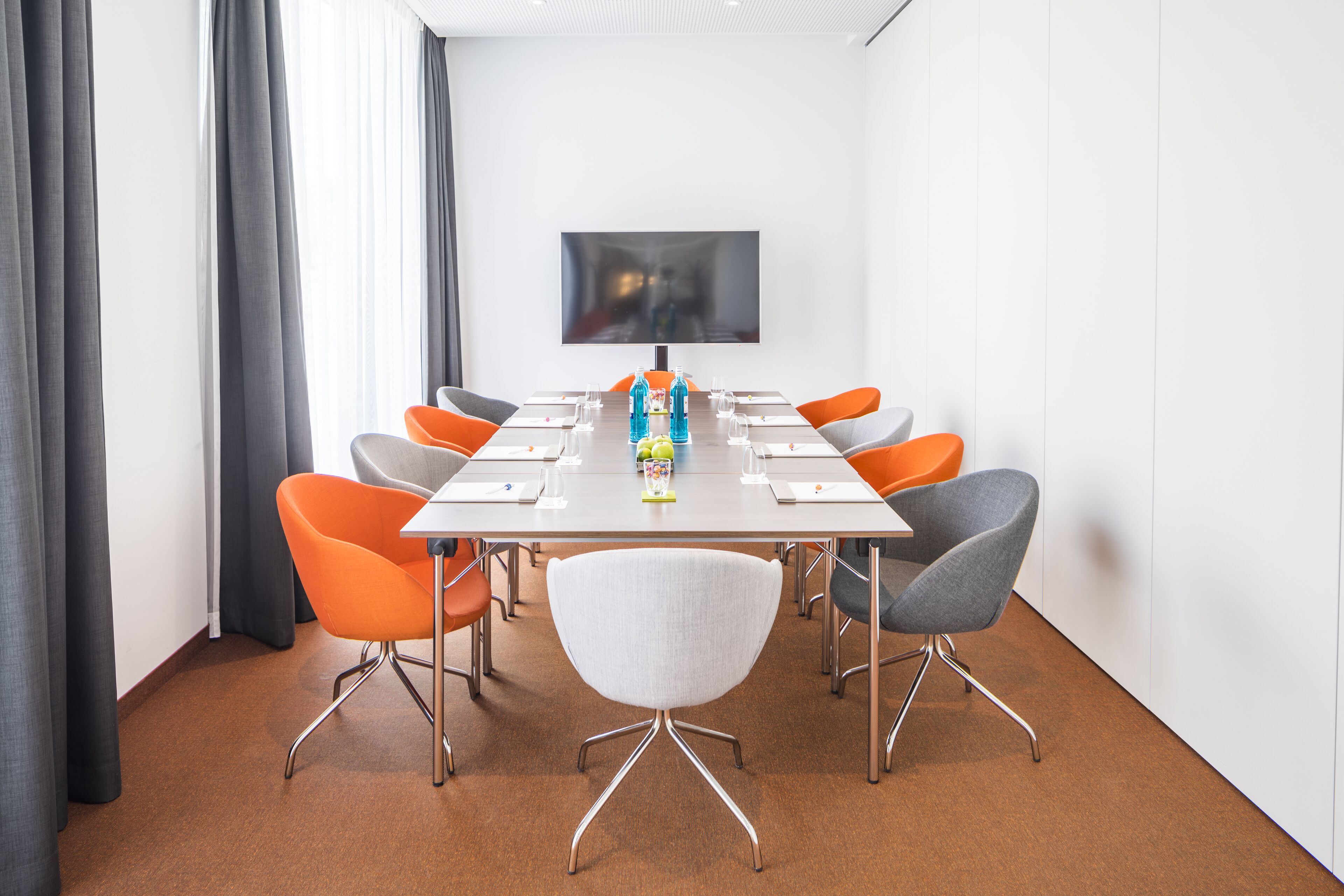 A conference room with a long table, six chairs, and a large screen on the wall.