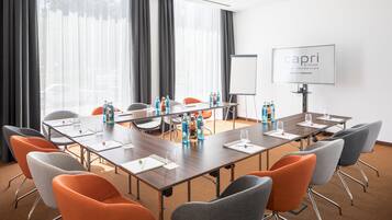 Une salle de conférence avec une longue table, de nombreuses chaises, des bouteilles d’eau et un tableau blanc.