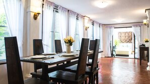 A dining area with a wooden table and chairs, a vase with flowers, and a view through the window. - Rachamankha Thai Villa (Chiang Mai)