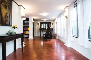 A spacious hallway with a polished wooden floor, a dining area with chairs and a table, a bookshelf, and a painting on the wall. - Rachamankha Thai Villa (Chiang Mai)