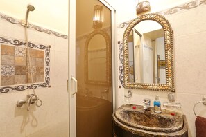 A bathroom with a shower, a sink with a decorative basin, and a mirror with an ornate frame.