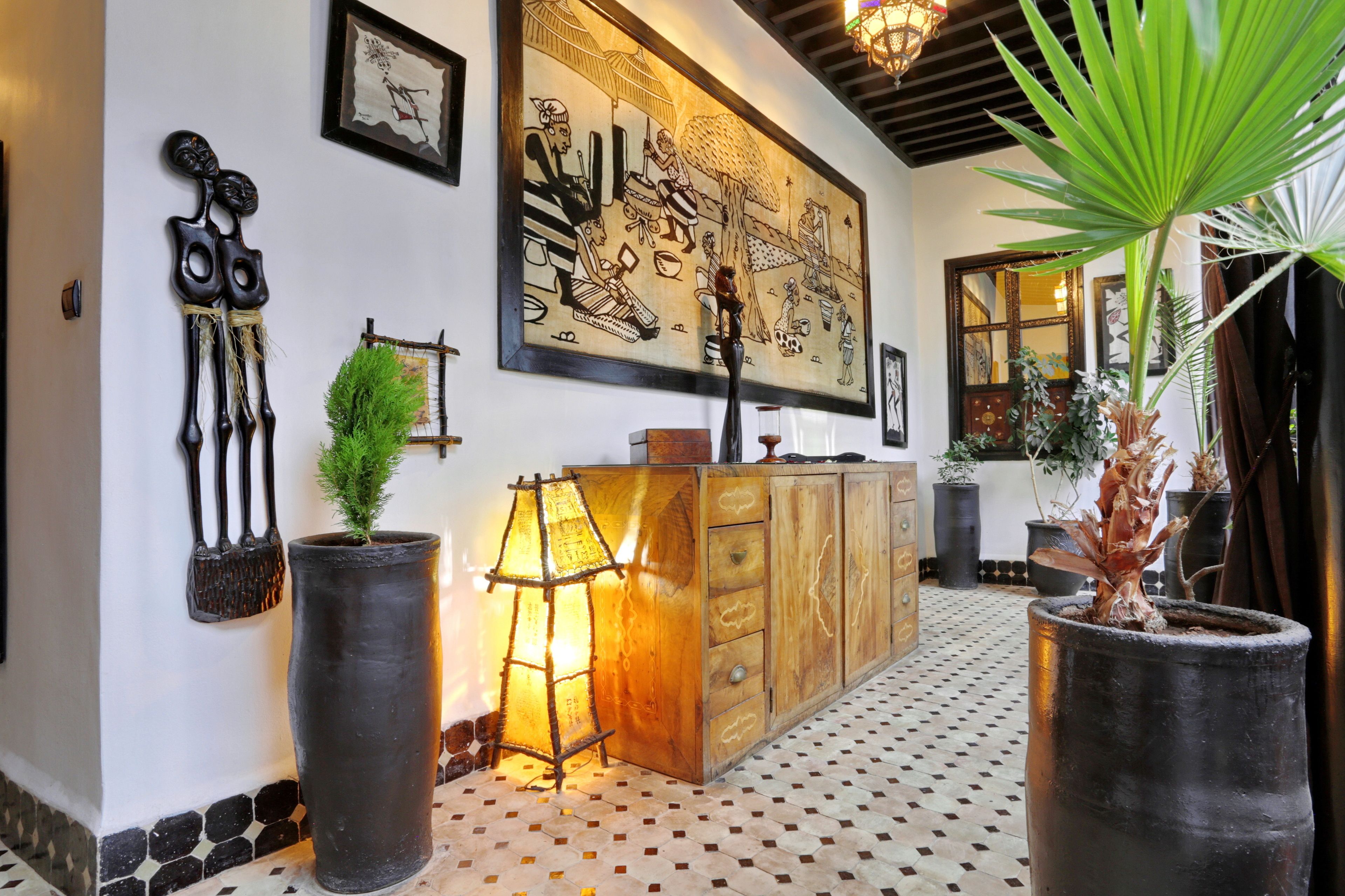 A hallway with a tiled floor, a wooden cabinet, a large wall mural, and potted plants.