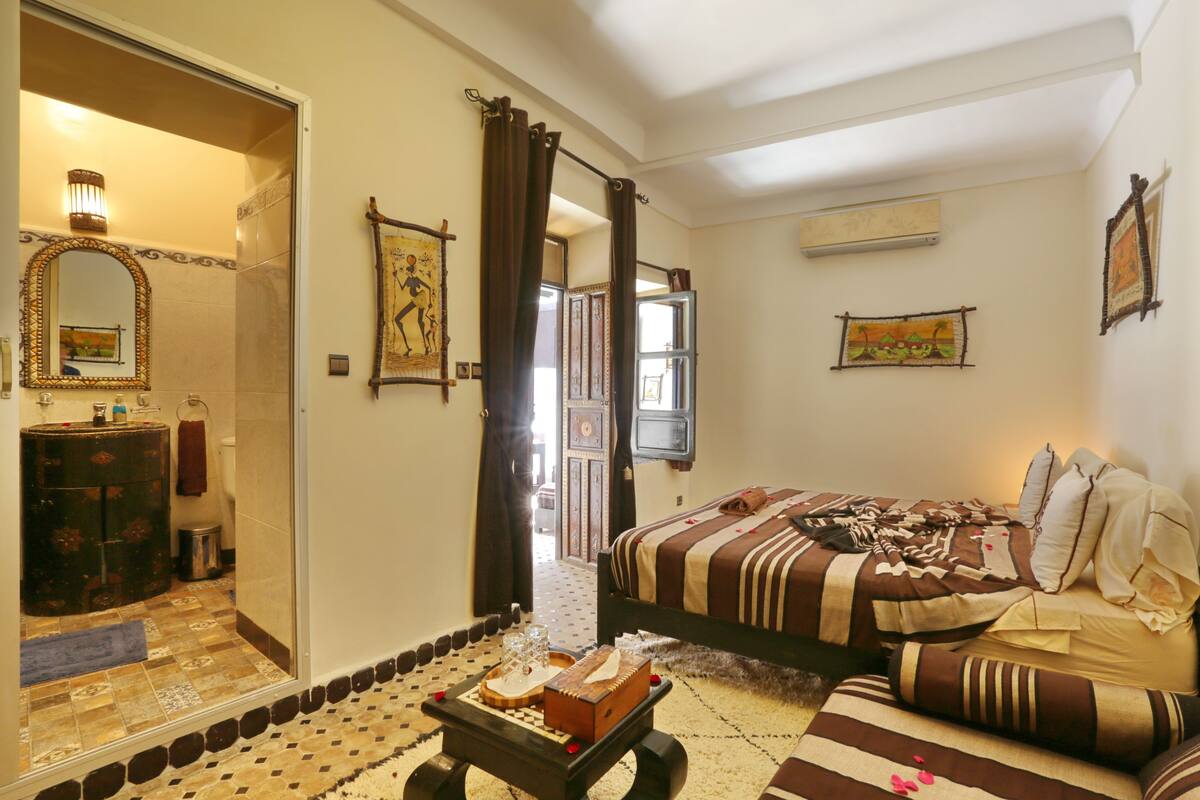 A hotel room with a bed, a desk with a mirror, a bathroom, and a view of the outside.