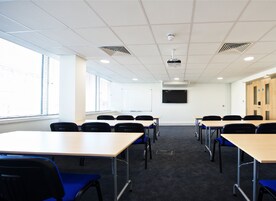 A conference room with tables and chairs, a projector, a screen, and windows with blinds.