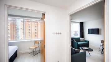 Una habitación de hotel moderna con un ventanal grande, un sofá, una mesita y un televisor montado en la pared.