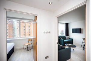 Una habitación de hotel moderna con un ventanal grande, un sofá, una mesita y un televisor montado en la pared.