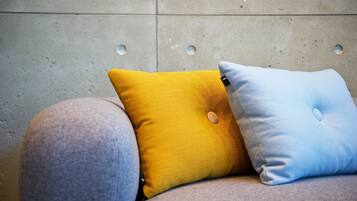 A sofa with two cushions, one yellow and one blue, against a textured wall with circular indentations.