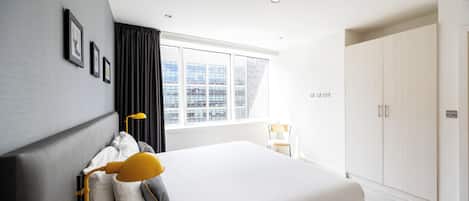 A modern bedroom with a large bed, a window with curtains, a wardrobe, and a desk with a chair.