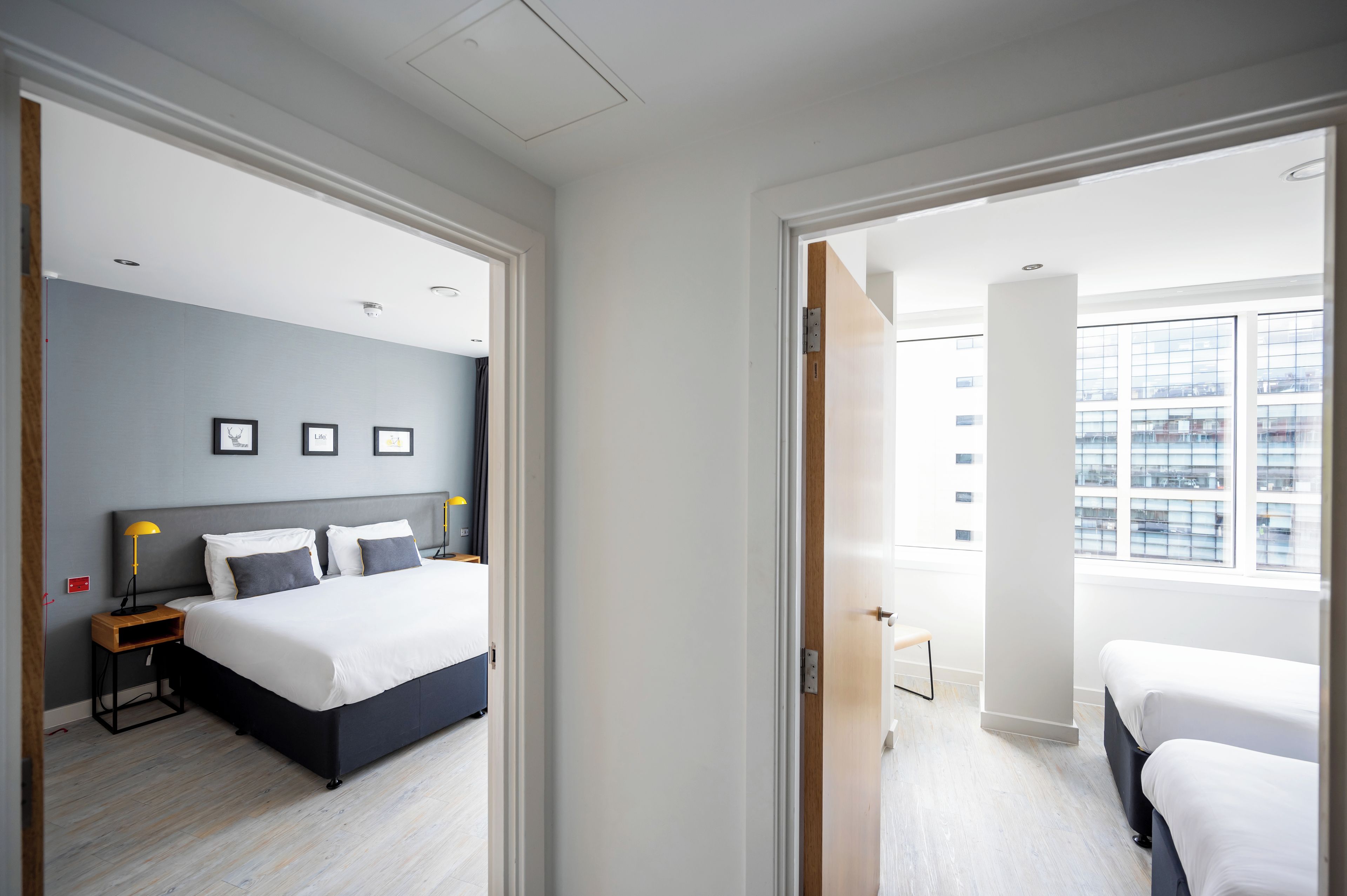 A hotel room with a bed, bedside tables, a lamp, and a view of the city through large windows.