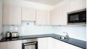 Una cocina moderna con armarios de madera clara, un lavamanos de acero inoxidable, un horno empotrado y un microondas.