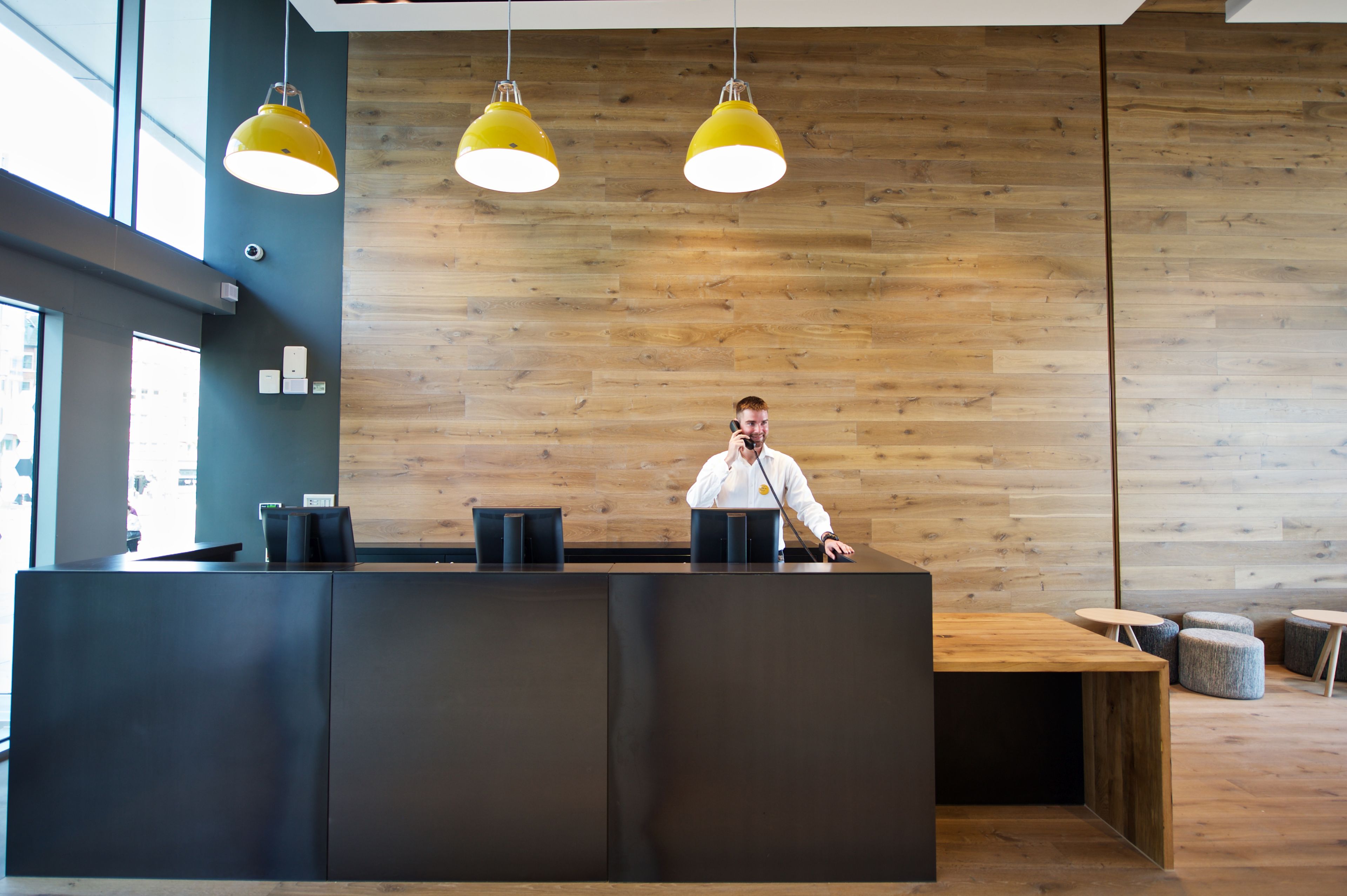 A reception desk with a wooden wall background, a modern pendant light, and a view of the street outside.