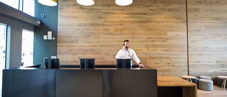 A reception desk with a wooden wall background, a modern pendant light, and a view of the street outside.