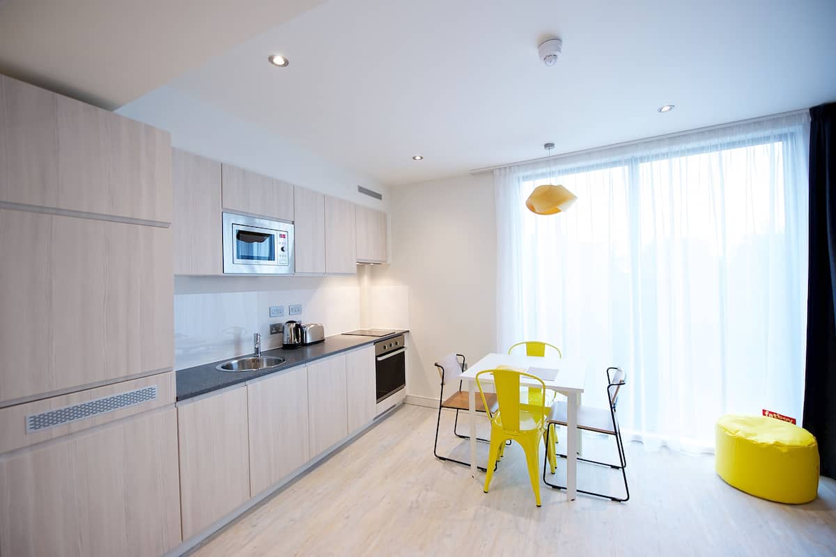 A modern kitchen with light wood cabinets, a microwave, and a dining area with a white table and yellow chairs.