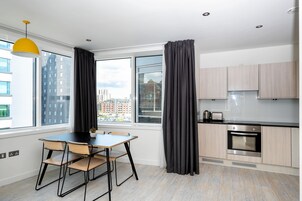Una cocina moderna con horno empotrado, comedor con mesa y sillas, y ventanas amplias con cortinas.