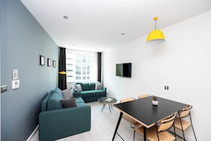 A modern living room with a sofa, a dining table, and a TV mounted on the wall. - Staycity Aparthotels, Manchester, Piccadilly (Manchester)