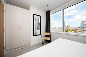 Una habitación de hotel moderna con un ventanal grande, un armario de madera, una silla y una cama.