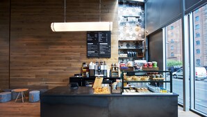 Interior moderno de cafeteria com parede de madeira, um quadro de cardápio e um balcão exibindo doces e café.