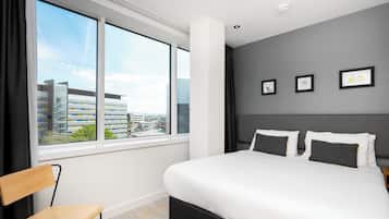 A modern hotel room with a large bed, a view of the city, and three framed pictures on the wall.