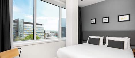 A modern hotel room with a large bed, a view of the city, and three framed pictures on the wall.