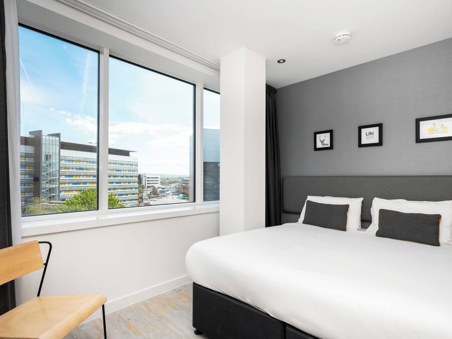 A modern hotel room with a large bed, a view of the city, and three framed pictures on the wall.