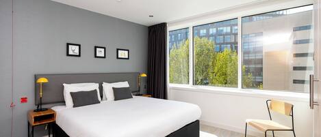 Et moderne hotelværelse med en stor seng, et skrivebord, en stol og et vindue med udsigt over byen.