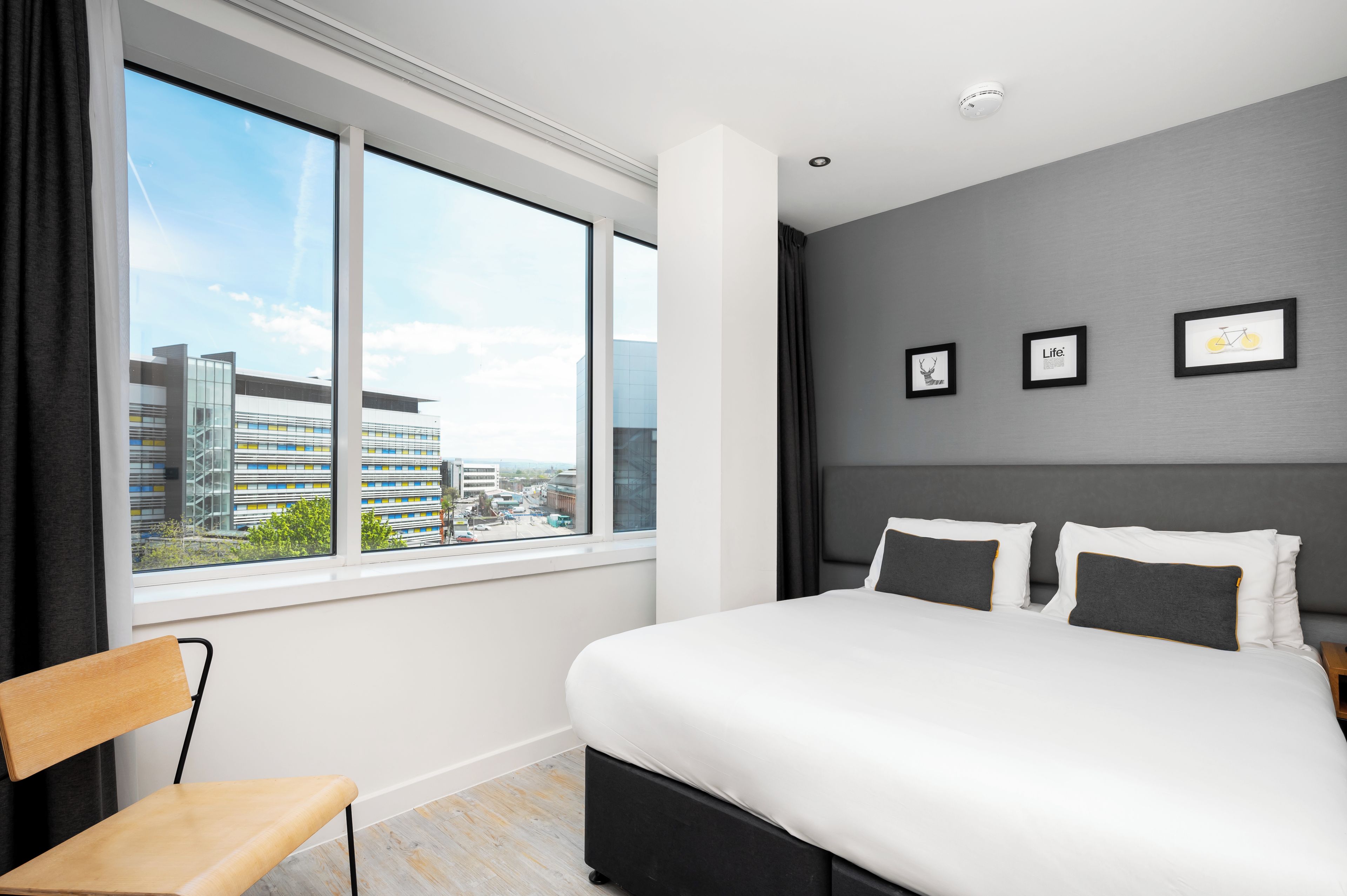 A modern hotel room with a large bed, a view of the city, and three framed pictures on the wall.