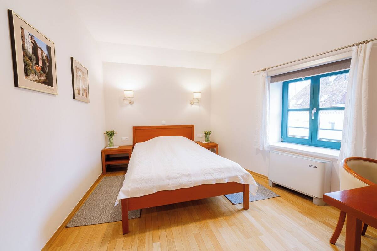 Une chambre à coucher avec un lit, des tables de chevet, une fenêtre avec des rideaux et un radiateur.
