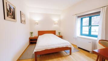 A bedroom with a bed, bedside tables, a window with curtains, and a radiator.
