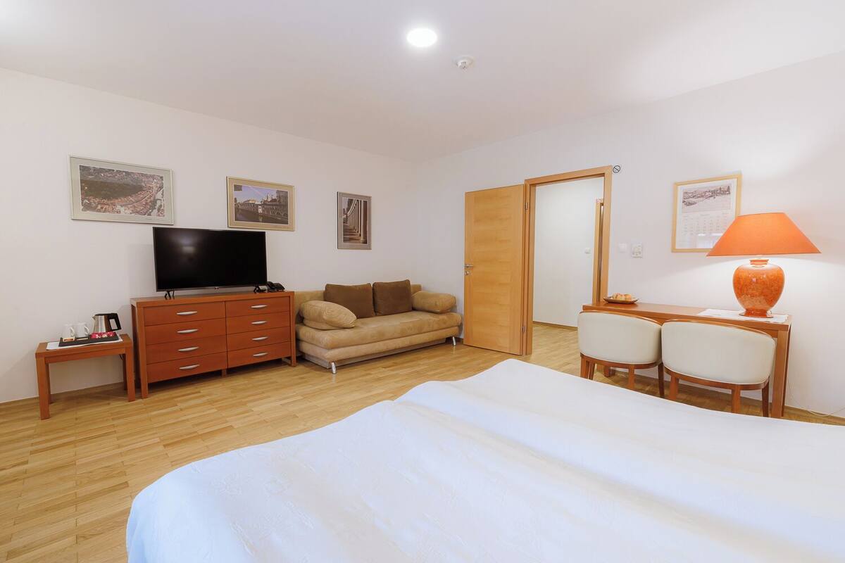 Une chambre d’hôtel comprenant un lit, une télévision, un canapé, un bureau avec des chaises et une armoire en bois.