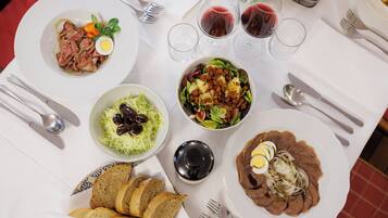 A table set with various dishes, including meat, vegetables, and bread, along with wine glasses and cutlery.