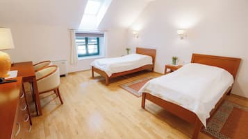 A bedroom with two beds, a desk, a chair, a window with curtains, and wall-mounted lights.