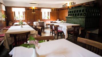 A restaurant with wooden walls and tables set with white tablecloths. There are chairs around the tables, and a green cabinet is visible in the background.
